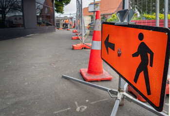 Man Walking Road sign along a closed footpath. Unrecognizable workers in the distance. Roadworks in...