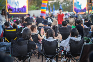 Crowd of people are sitting in chairs at a concert. Scene is lively and energetic, Summer festival...
