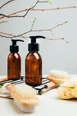 Set of natural cosmetics. Amber bottles with facial, bath liquid on a concrete background with young twigs of a tree. Front view - obrazy, fototapety, plakaty