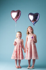 Children, holding hands and sister with heart balloon in studio on blue background for family or party. Birthday, celebration event or happy with smile of girl kids on color backdrop together