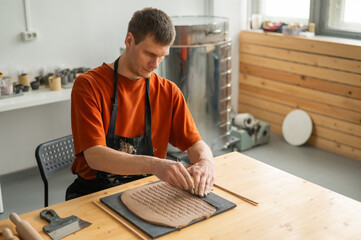 A potter cuts a piece of rolled clay with patterns. 