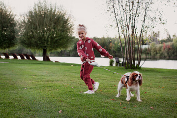 Blonde Girl Running and Playing with playful Spaniel Pet Outdoors. candid moment Happy child with dog in motion