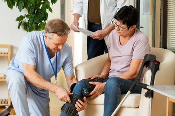 A male nurse helps to put a bondage, medical splint, knee brace on the leg of an elderly female patient who communicates with the attending physician at the clinic or hospital. Signing insurance