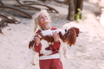 Beautiful blond girl child hugs and plays with a dog on the beach in summer, enjoying outdoor fun and affectionate moments - obrazy, fototapety, plakaty