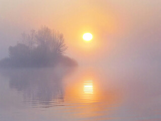 Soft pink and orange light filters through fog over calm lake, creating serene morning atmosphere.