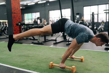 Male gymnast doing tagged out handstand. Strong muscular fit man standing on hands holding on push-up stop. Athletic male taking static pose to strengthen cortical muscles during training in gym.