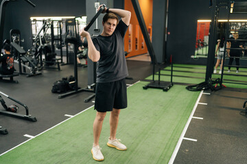 Full length portrait of beginner sportsman holding and rotating weight disc plate overhead during sport workout training in modern gym. Concept of healthy lifestyle, physical sport activity.