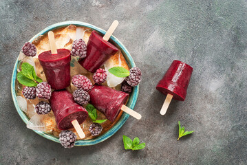 Berry popsicles in a plate with ice and mint leaves on a rustic background. Summer refreshing cooling dessert. Fruit frozen juice on a stick.