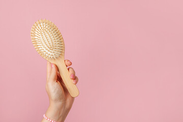 Woman hand holding wooden hairbrush on pink background, copy space