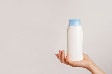 Woman hand holding white bottle of shampoo or hair conditioner on white background, copy space