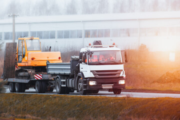 Flatbed Truck delivering heavy machinery to the construction site. Excavator tractor or crane. Construction industry.