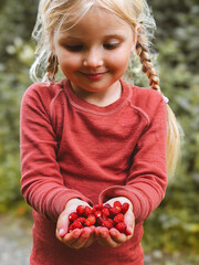 Child girl hands giving wild strawberries freshly picked berries in forest summer vacations seasonal harvest, vegan healthy food