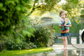 Cute little boy playing with garden hose on hot summer day. Child playing with water at summertime. - 794964984