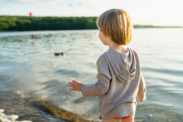 Cute little boy playing by a lake or river on hot summer day. Adorable child having fun outdoors during summer vacations.
