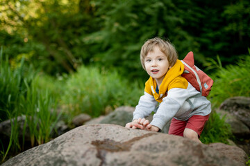 Cute little boy with a backpack having fun outdoors on sunny summer day. Child exploring nature. Kid going on a trip. - 794973159