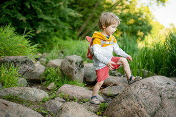 Cute little boy with a backpack having fun outdoors on sunny summer day. Child exploring nature. Kid going on a trip. - 794973358