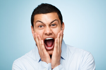 Portrait, screaming and man with surprise, excited and expression on blue studio background. Face, person and model with shock, shouting or wow with emotion, reaction or omg with celebration or smile - obrazy, fototapety, plakaty