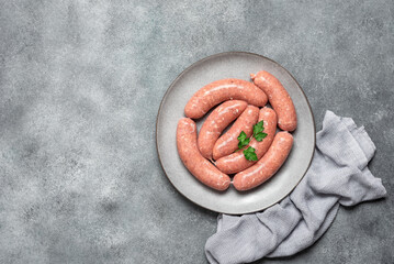 Raw homemade sausages in a plate on a gray concrete background. Top view, flat lay, copy space.