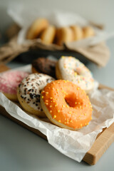 Orange glazed donut with other colors in background on a wooden plank light background. Desert Snack. Vertical.