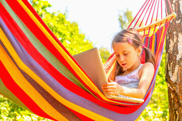 Young beautiful girl relaxing in hammock while working on laptop. She learning and communicates online remotely. Horizontal image.