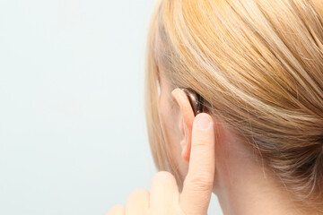 Woman wearing digital hearing aid. Person with disability from the back, medical support, listening and healthcare technology. Deafness treatment, hearing solutions. Place for text.