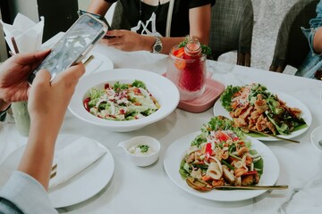 People enjoying a meal together at a restaurant, with one person taking a photo of their food, suitable for social media or dining promotions.