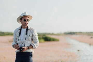 Man with a camera wearing a hat and sunglasses standing in a serene natural setting, evoking a...