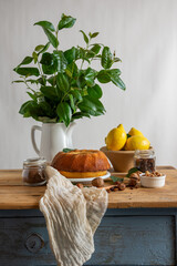 View of rustic kitchen table with bundt of lemon, walnuts, hazelnuts, cloth and jug with green bouquet, white background, vertical, with copy space - obrazy, fototapety, plakaty