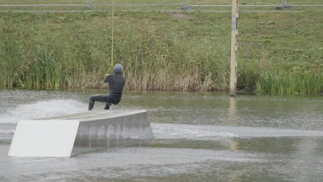 Back view shot of male wakeboarding rider practicing on slider in outdoor wake cablepark