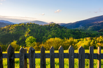 weathered wooden fence. mountainous rural landscape of transcarpathia, ukraine in spring blurred in the distance. carpathian countryside with forested rolling hill beneath a blue sky in evening