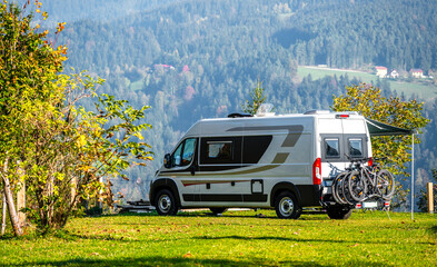 Campervan or motorhome with bicycle rack parked in the nature countryside. Camper van or  motor home is camping in a meadow surrounded by forest and hills. Active family vacation in Slovenia.