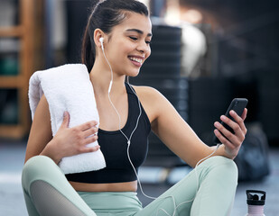 Earphones, gym and woman with phone, watch and video of fitness, exercise and online for wellness. Technology, mobile and social media for happiness, person and athlete on break, relax and towel