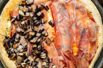 inquadratura dettagliata con visuale in primo piano e dall'alto di una pizza fatta in casa, condita e farcita con prosciutto crudo e pezzi di radicchio