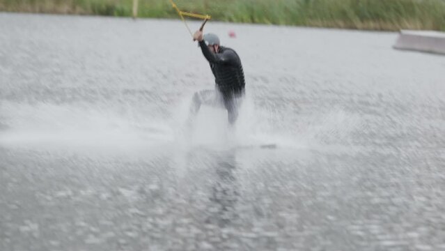 Slowmo shot of Caucasian adult wakeboarder in helmet and wetsuit practicing front roll trick from slider and falling into water