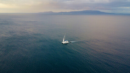 The catamaran is sailing on a calm, endless sea against the backdrop of a tropical island. Aerial...