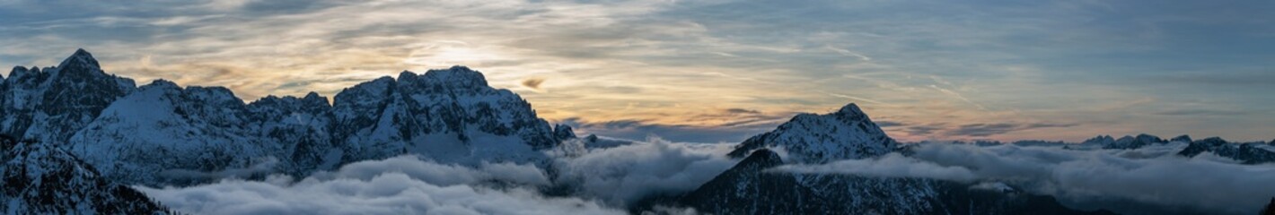 ampia composizione panoramica di immagini multiple che mostra dall'alto un bellissimo ambiente naturale di montagna innevato, in inverno, al tramonto, nel nord est italia,