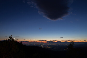 ampia visuale panoramica che mostra dall'alto sulla cima di una collina varie città e paesi distanti vicino a Udine, nel nord est Italia, di sera, al tramonto, sotto un cielo parzialmente sereno