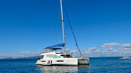 A sailing catamaran stands at sea. A catamaran with a folded sail stands in a parking lot on the...