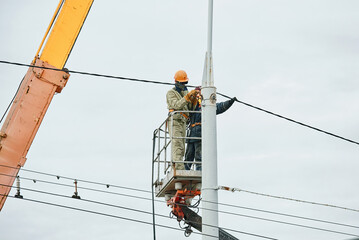 Construction workers in crane bucket welding street light pole. Street light repair works, workers team repair street lamp at height, teamwork. Men in lift bucket work with blowing torch