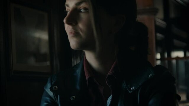 Young woman, sitting in a dark moody pub looking around, portrait, cinematic. 