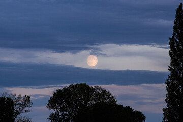 vista in primo piano della luna piena, dietro le nuvole color blu, di sera, al tramonto e dietro le...