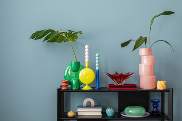 Colorful composition on blue wall with black shelf, design accessories, and decorations  vases with leaf, candels and copy space. Home decor. Template.