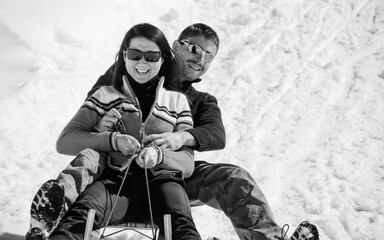 A caucasian couple has fun going downhill on a wooden sled in the snow