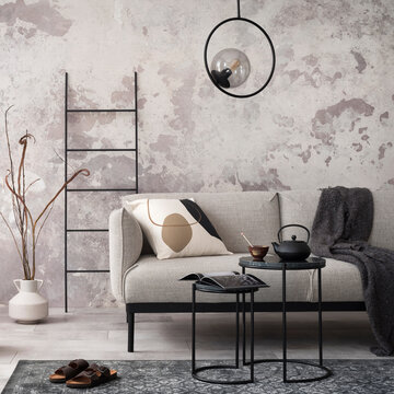 Loft style of modern apartment with grey design sofa, black coffee table, black ladder, pedant lamp, carpet, wooden decoration and elegant accessories . Concrete grunge wall. Template.