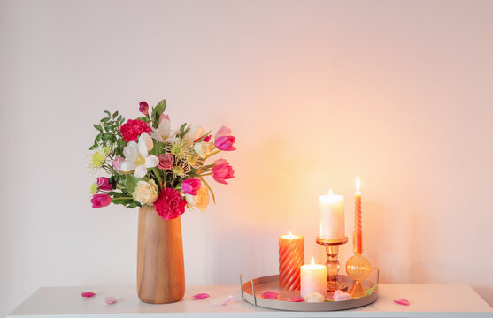  flowers  in vase and burning candles on shelf  on background wall