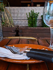 Knife and fork with black handles and a napkin on an empty, eaten plate with leftovers on a table with an empty glass and the background of a simple restaurant.