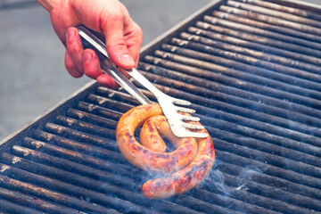 Male hand with a fork touching sausage on the grill - 795082367
