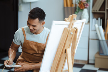 young male artist painting on canvas in the home studio, fine arts and creativity concept.