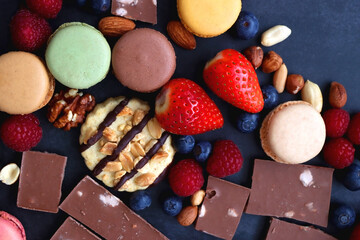 Macarons, chocolate, cookies, berries and various nuts on dark blue background. Top view.