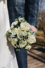 groom holding a wedding bouquet of white roses